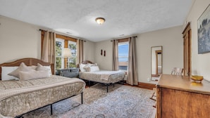 Une chambre avec deux lits, une commode en bois, un miroir et une vue sur l’extérieur.