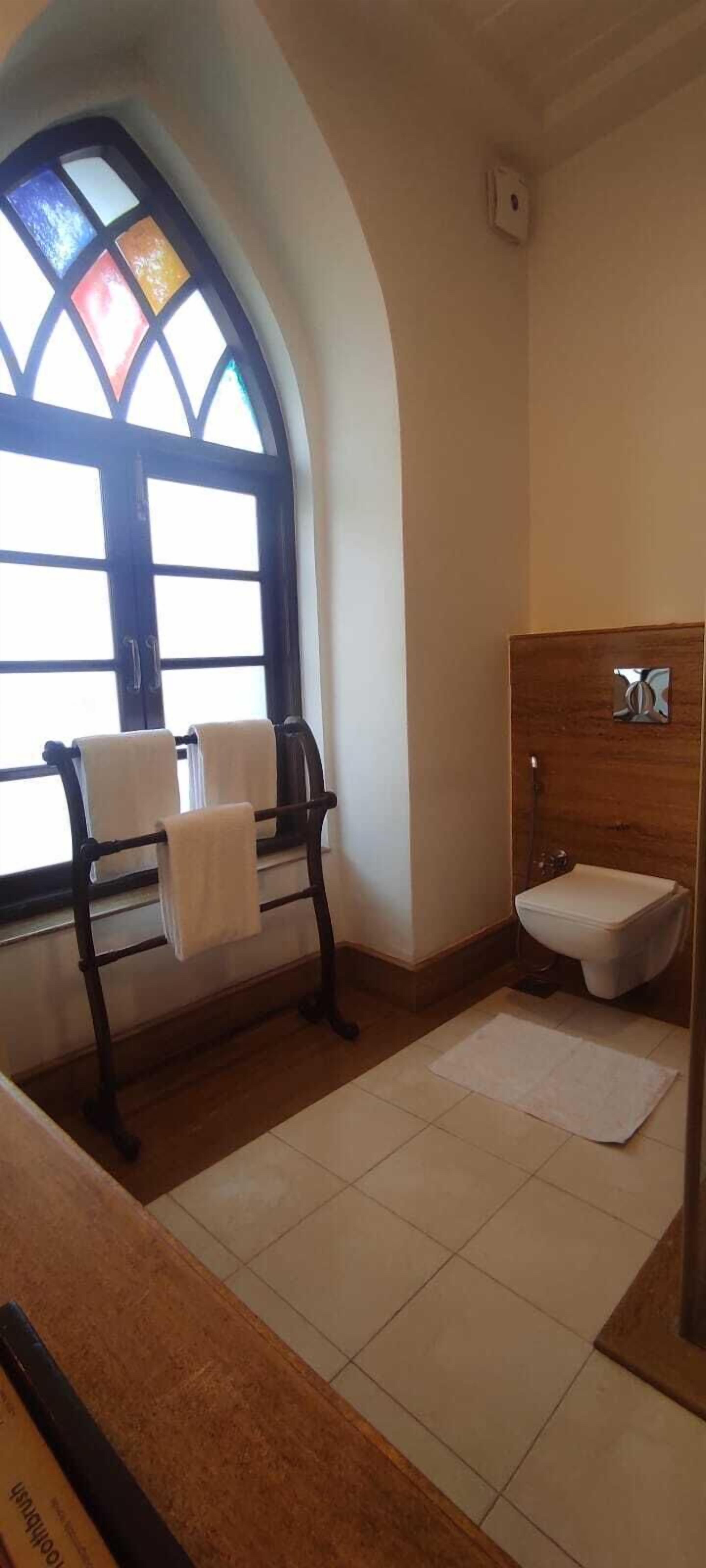 A bathroom with a large arched window, a wooden vanity, a white sink, and a towel rack with two towels.