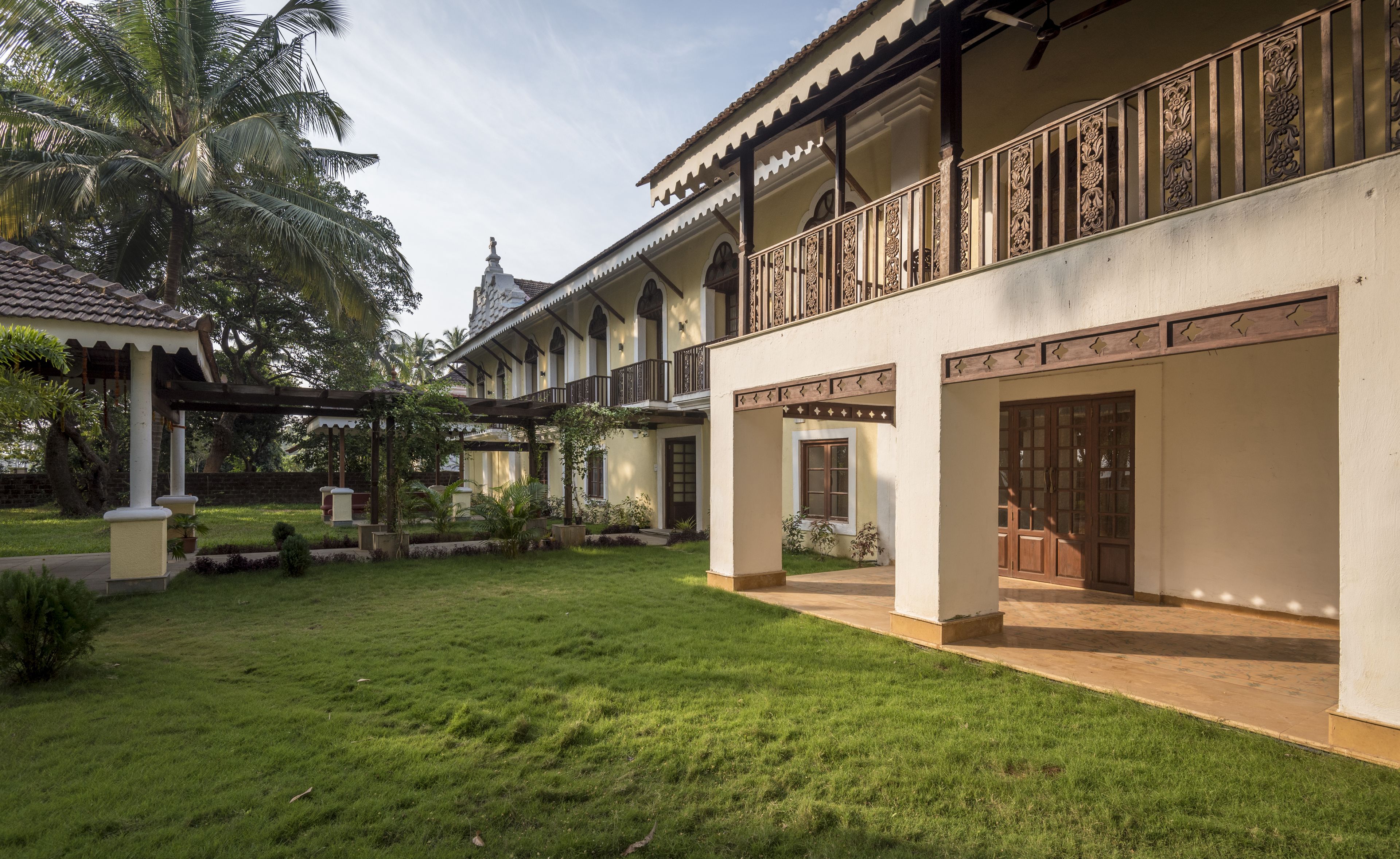 A traditional building with a covered courtyard, a balcony with ornate railings, and a well-maintained lawn.