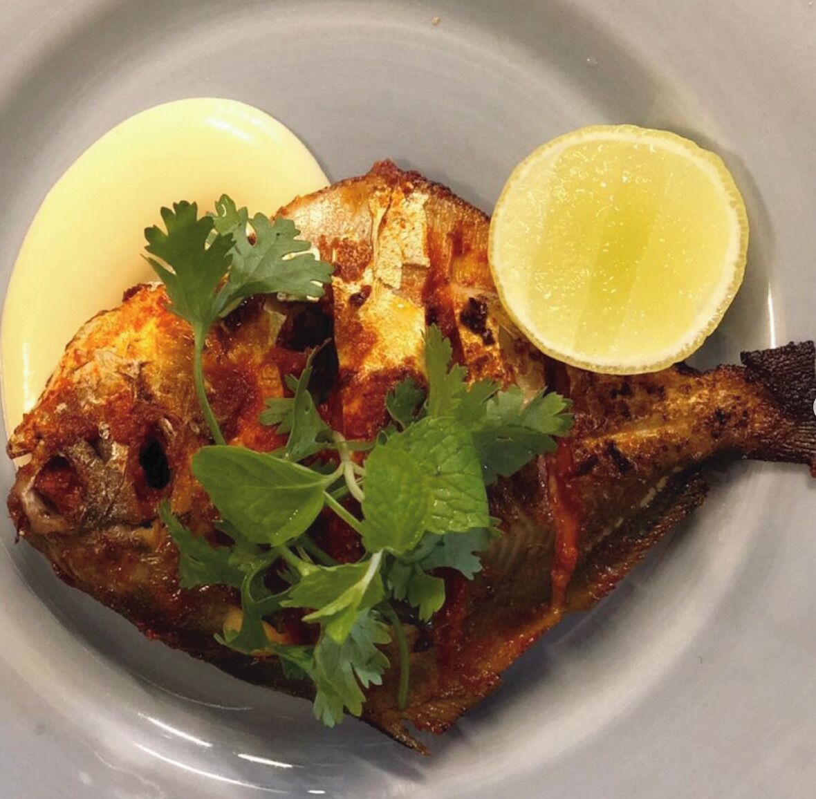 A whole grilled fish with lemon and cilantro garnish on a plate.