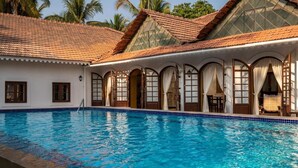 Una piscina con borde de azulejos, un patio cubierto con ventanales de arco y un techo también de azulejos.