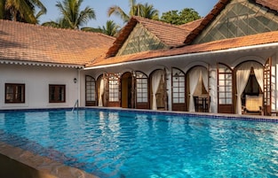Una piscina con borde de azulejos, un patio cubierto con ventanales de arco y un techo también de azulejos.