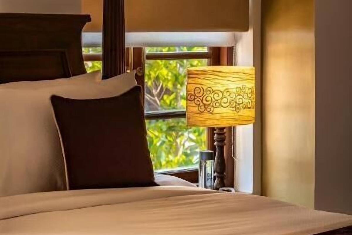 A bedroom with a bed, a nightstand, a lamp, and a stained glass window.