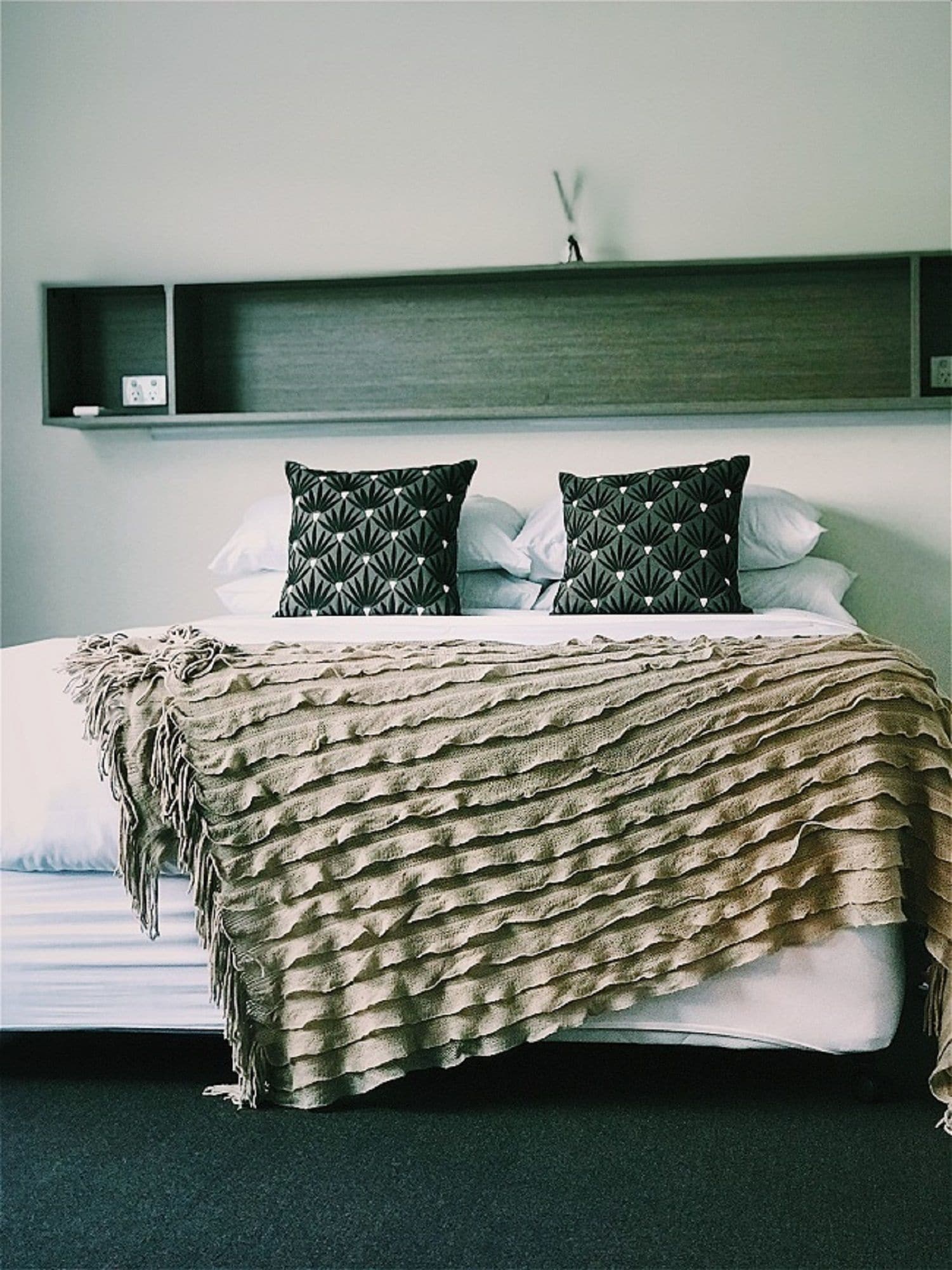 A bed with a textured blanket, two patterned pillows, and a dark headboard.