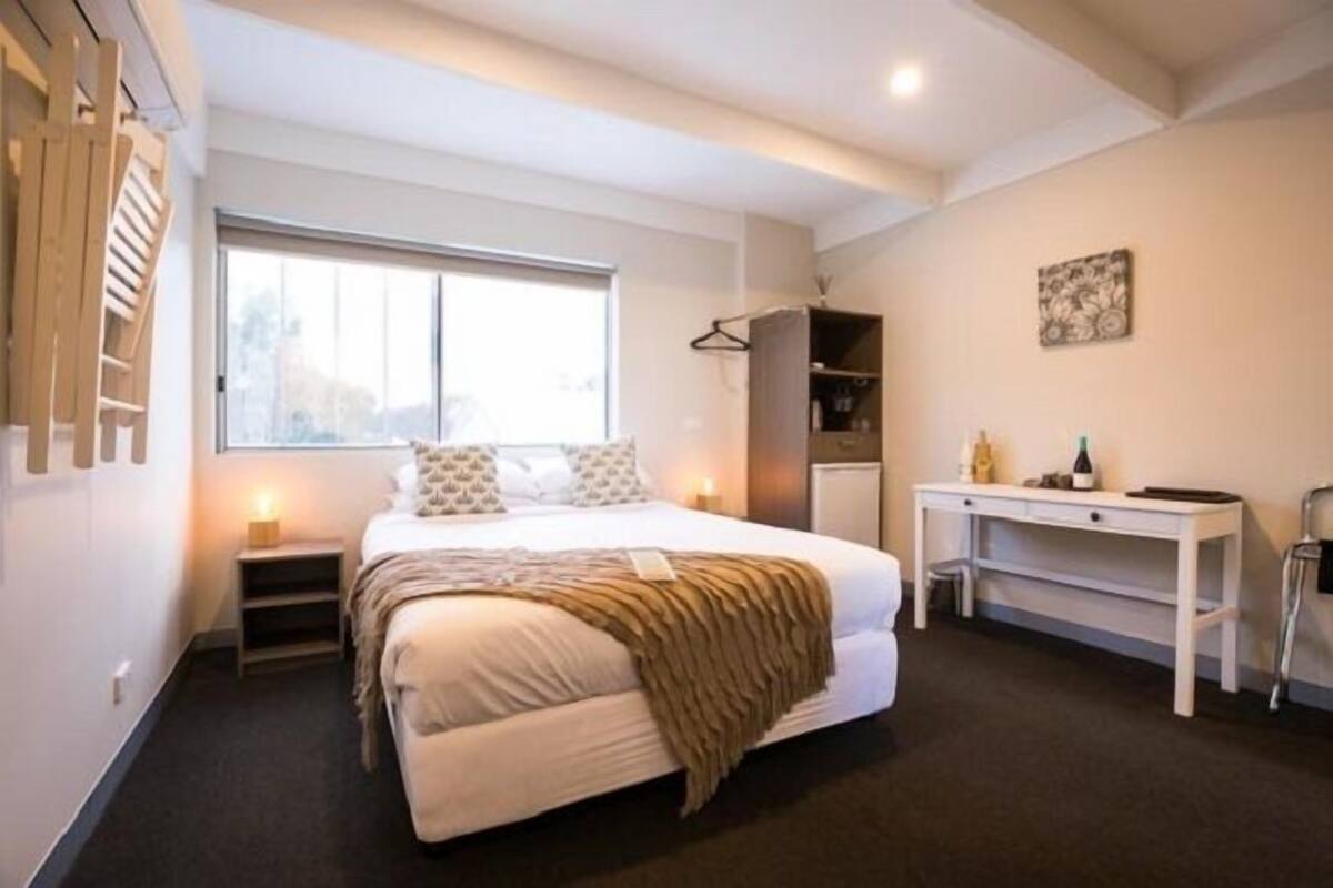Un dormitorio con cama, mesitas de noche, escritorio, armario y ventana.