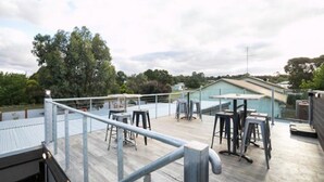 A rooftop terrace with metal railings, tables, and chairs.