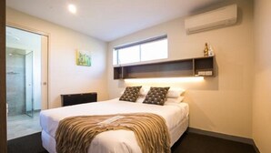 A hotel room with a large bed, a bedside table, a small desk, an air conditioning unit, and a window with a view.