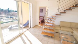 Ein modernes Wohnzimmer mit Glastür zum Balkon, einer Treppe mit Holzboden und einem beigefarbenen Sofa.