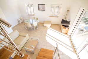 Un salon lumineux comprenant un canapé, une table basse, un téléviseur et une table à manger avec des chaises.