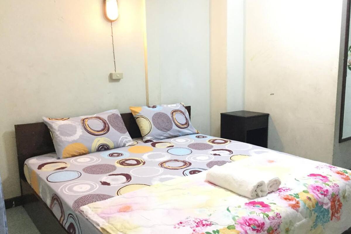 A neatly made bed with patterned bedding, a bedside table, and a wall-mounted light fixture.