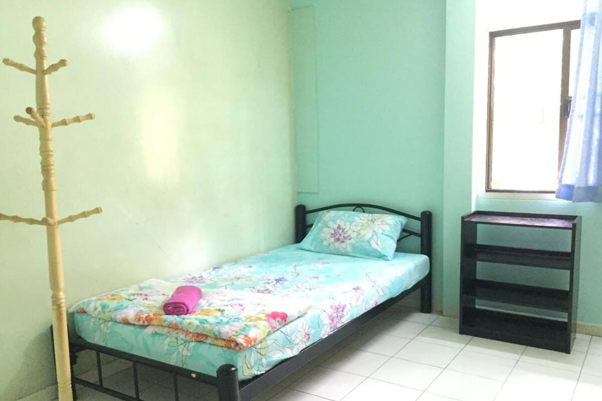 A small, single-bed room with a wooden bed frame, a floral bedspread, and a small table beside the window.