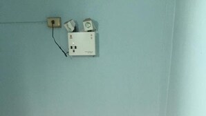 Ein Zimmer mit einer hellblauen Wand, einer weißen Stromdosenleiste mit Kabel und einem roten Feuerlöscher auf dem Boden.