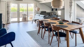 A spacious dining area with a wooden table and chairs, a sofa, and a large window with curtains. - Amazing home in Hemmet with sauna (Hemmet)
