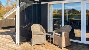 A covered outdoor seating area with wicker chairs and a table, a sliding glass door, and a wooden deck. - Amazing home in Hemmet with sauna (Hemmet)