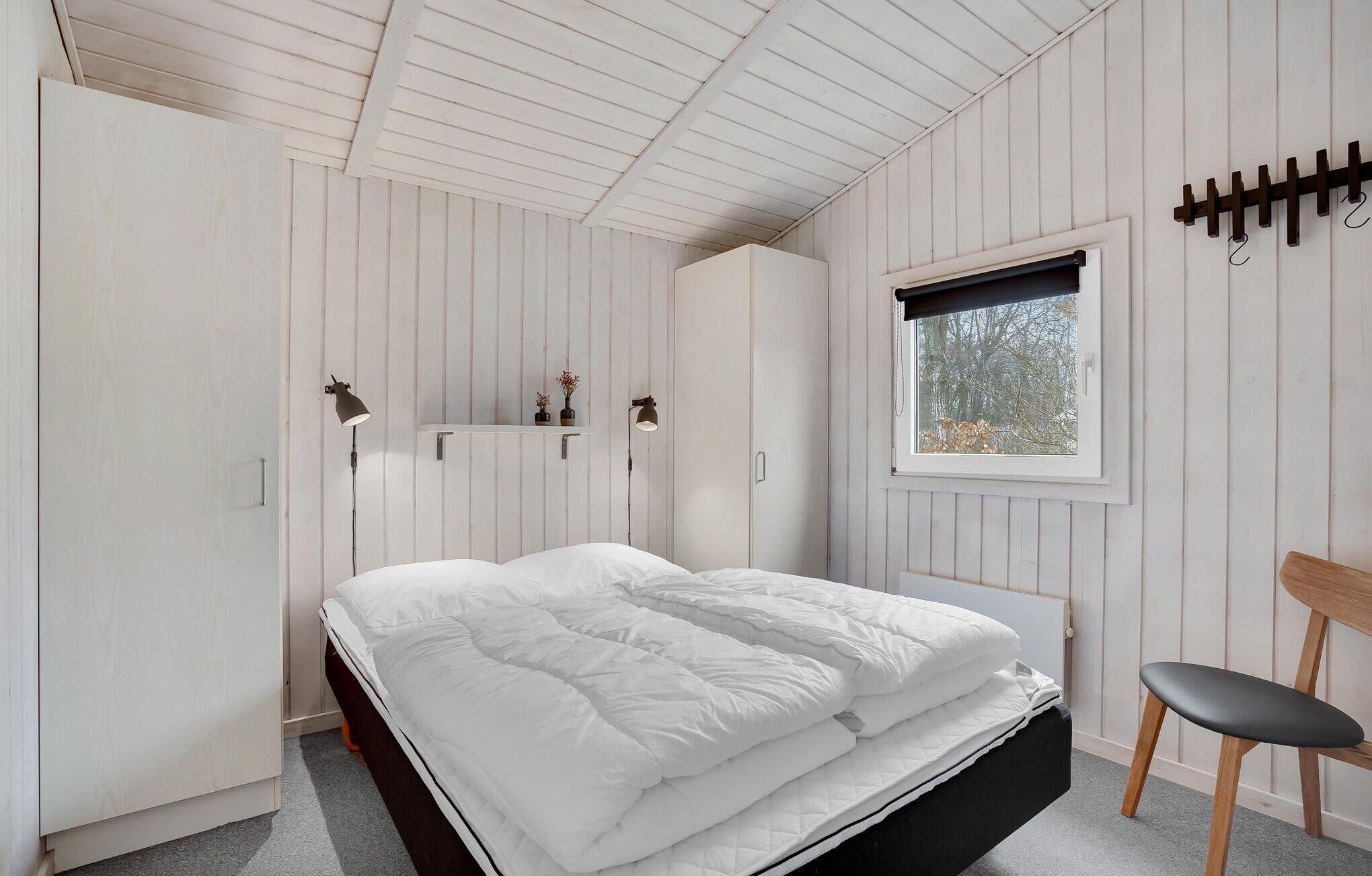 A bedroom with a bed, a window, a chair, and a wardrobe.