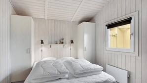 A bedroom with a bed, a wardrobe, a shelf with decorative items, a window, and a radiator. - Amazing home in Hemmet with sauna (Hemmet)