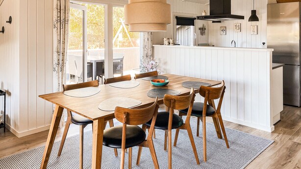 A dining area with a wooden table and chairs, a hanging light fixture, and a kitchen area with a refrigerator and stove. - Amazing home in Hemmet with sauna (Hemmet)
