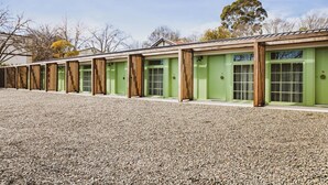 A row of green buildings with wooden accents, each with a door and windows, set against a gravel ground. - The Bowral Hotel (Bowral)
