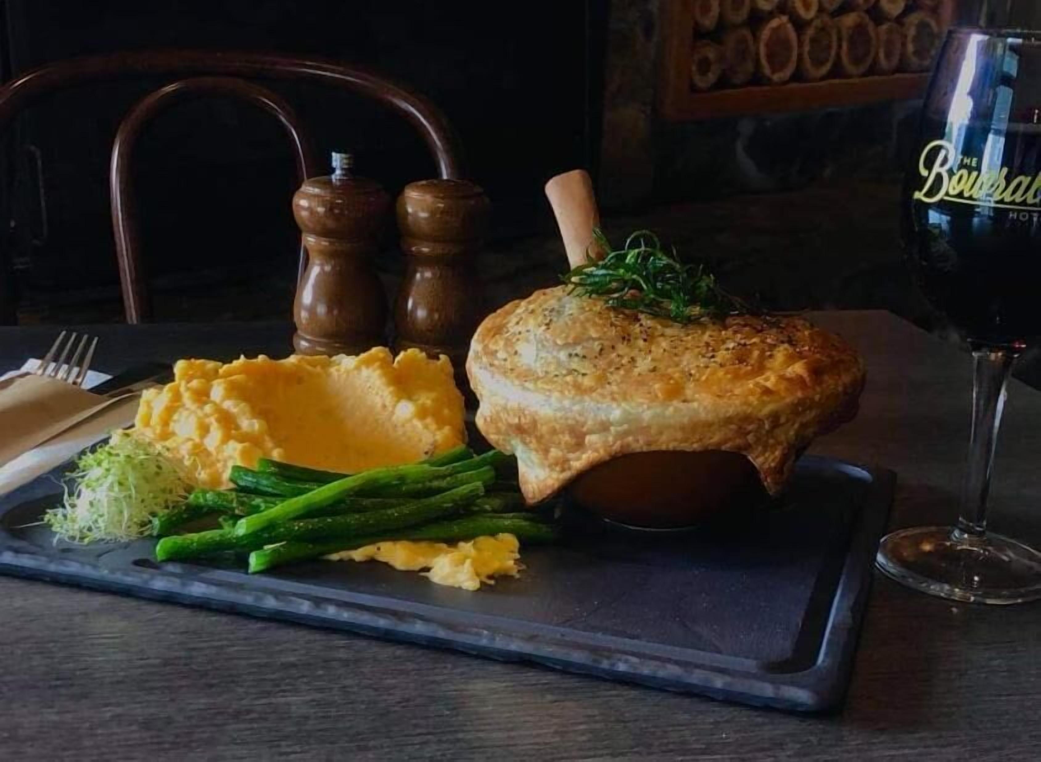 A meal consisting of mashed potatoes, asparagus, and a meat dish, served on a slate board with a glass of red wine.