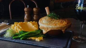 A meal consisting of mashed potatoes, asparagus, and a meat dish, served on a slate board with a glass of red wine.