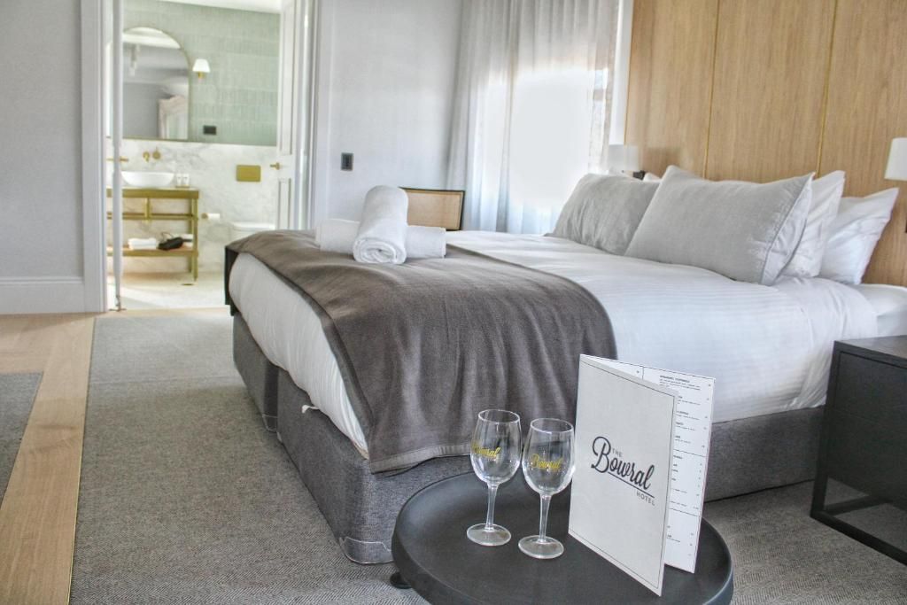 Une chambre d’hôtel avec un lit, une table de chevet sur laquelle reposent deux verres, un panneau et une vue sur la salle de bain.