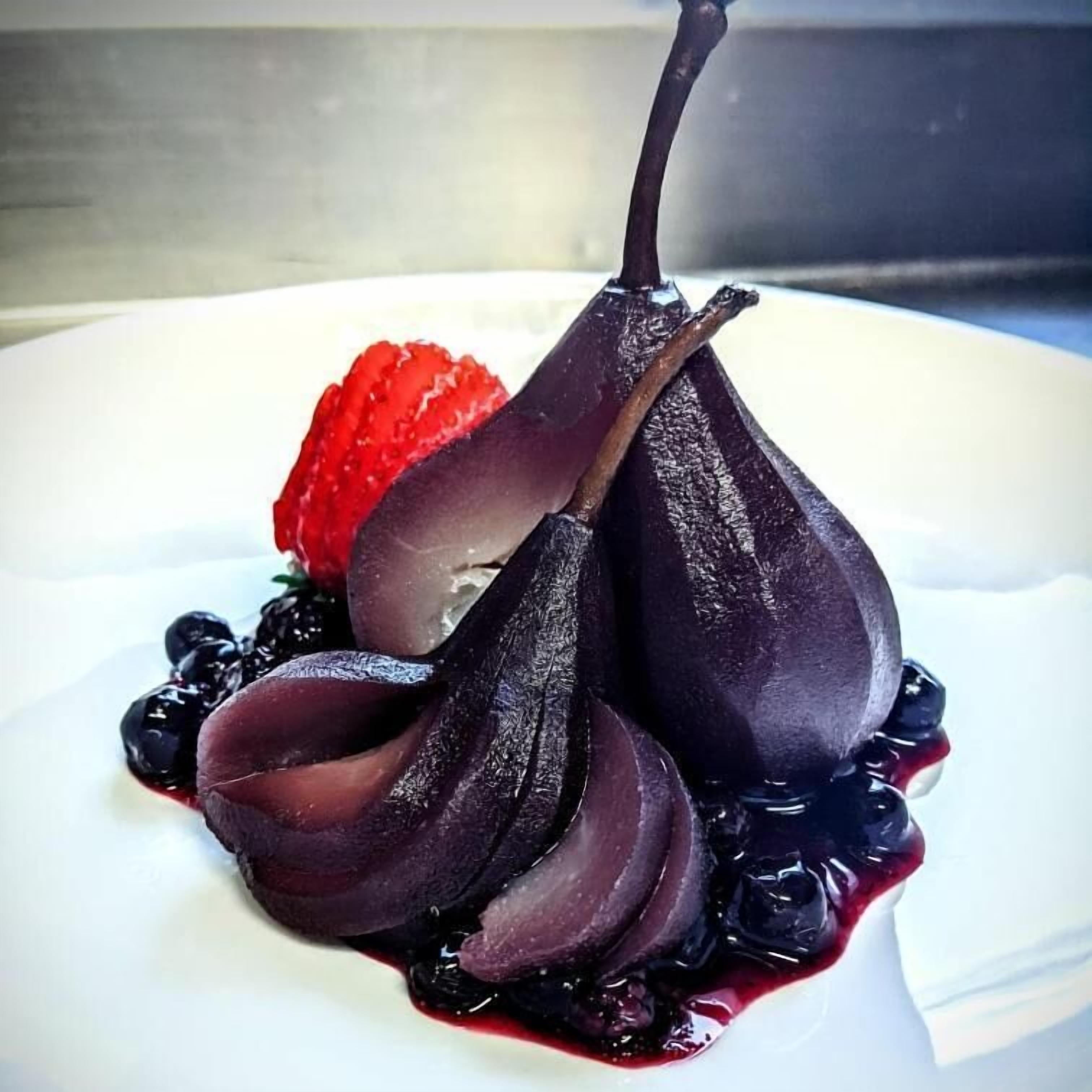 Un postre con una pera, arándanos y una fresa sobre un plato blanco.