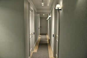 A hallway with doors on both sides, a carpeted floor, and wall-mounted lighting fixtures.