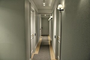 Un pasillo con puertas a ambos lados, piso alfombrado y lámparas fijadas en la pared.