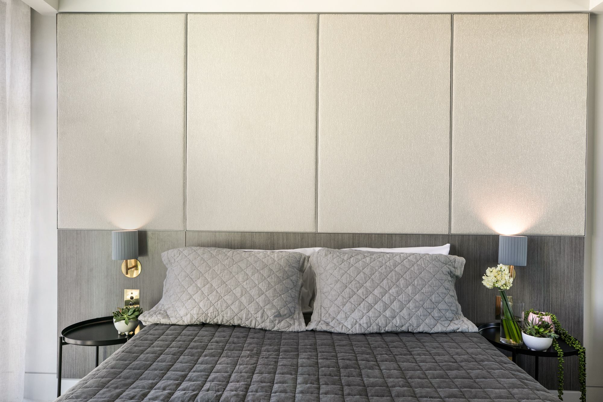 A modern bedroom with a large bed, two bedside tables, and a headboard with built-in lighting.