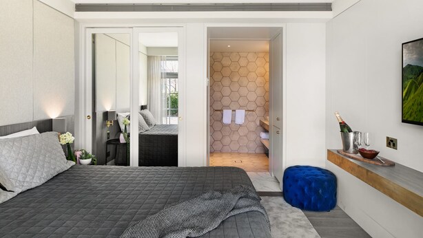 A modern bedroom with a large bed, a nightstand, a dresser, and a bathroom visible through an open door. - The Bowral Hotel (Bowral)