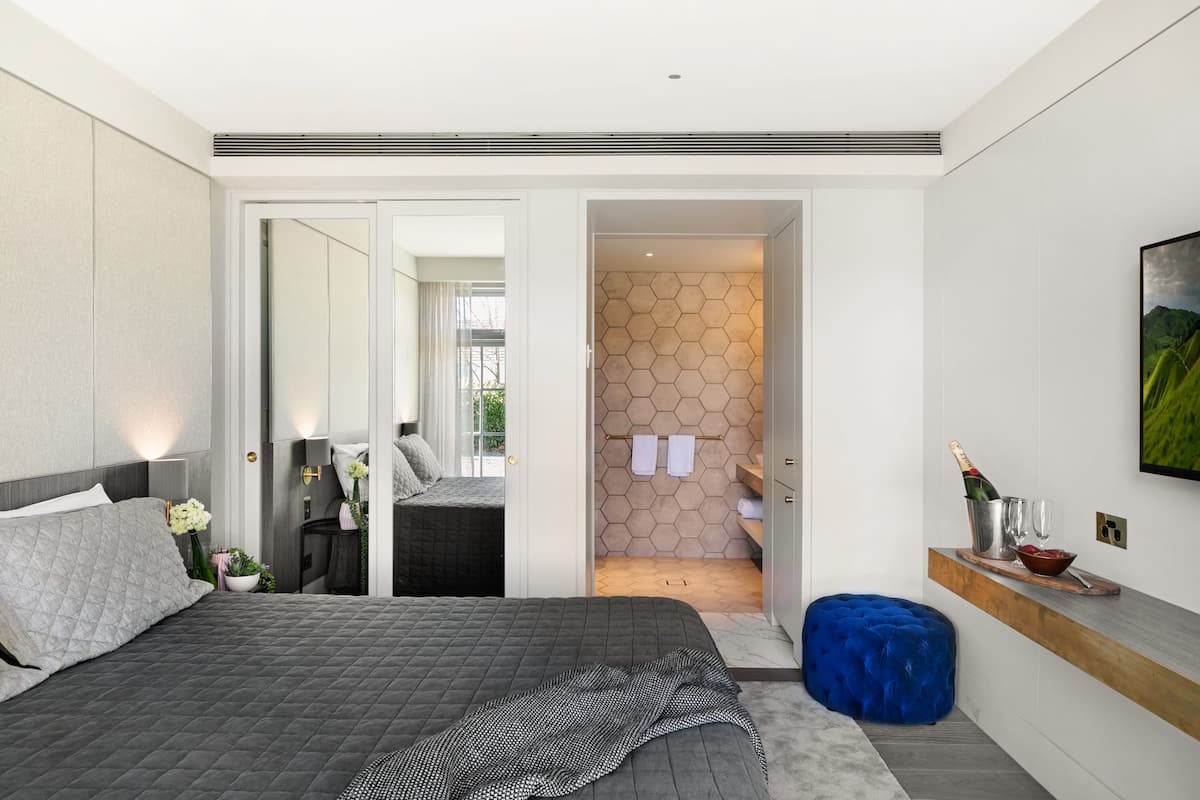 A modern bedroom with a large bed, a nightstand, a dresser, and a bathroom visible through an open door.