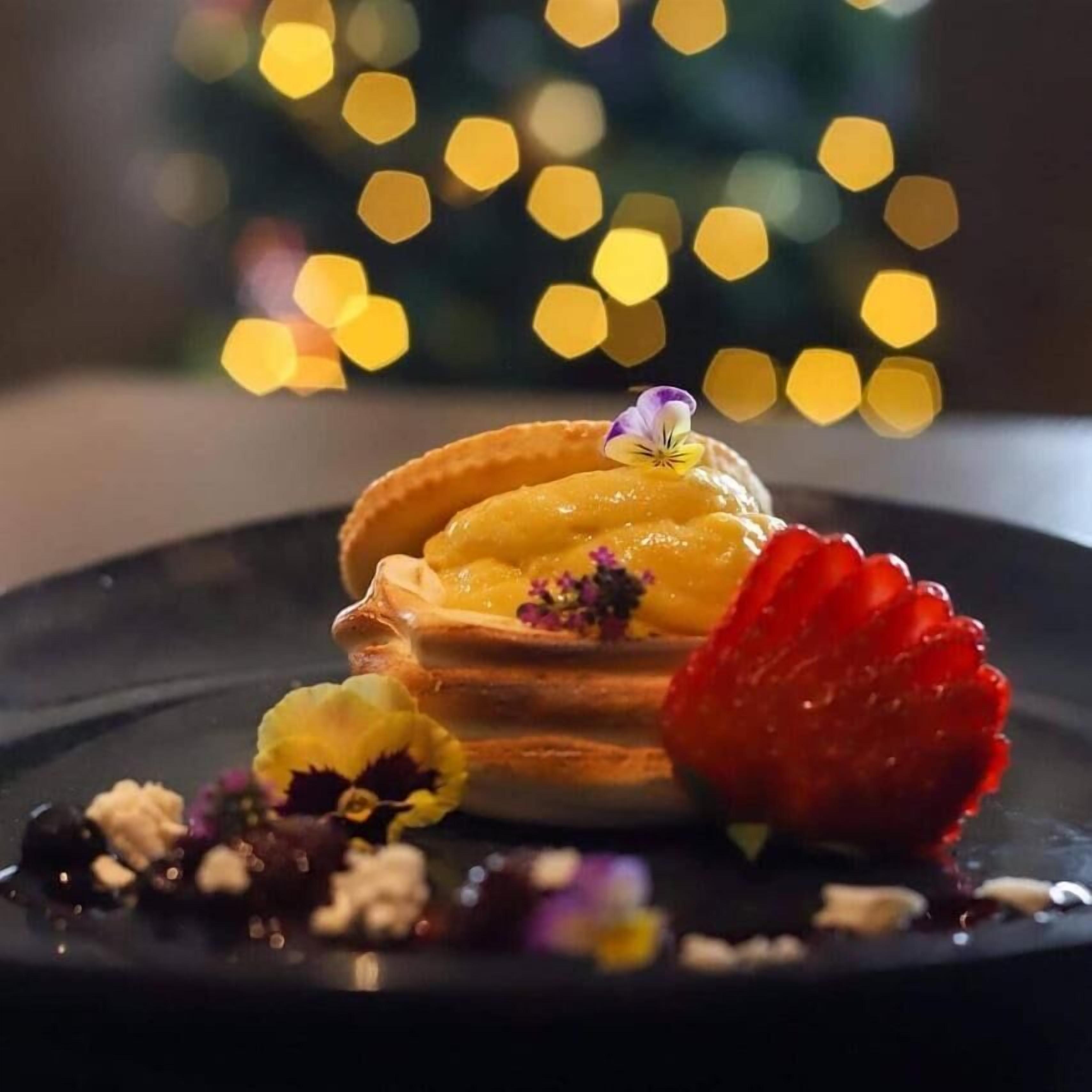 Un dessert composé d’une gaufre, de fruits et de fleurs décoratives, le tout présenté sur une assiette.