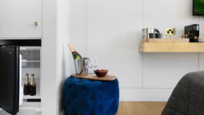 A modern kitchen with a black refrigerator, a blue velvet stool, a wooden side table with a bottle of champagne, glasses, and a bowl of strawberries. - The Bowral Hotel (Bowral)