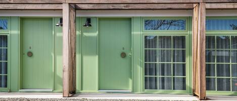 A building with three green doors and windows, wooden pillars, and a gravel driveway.