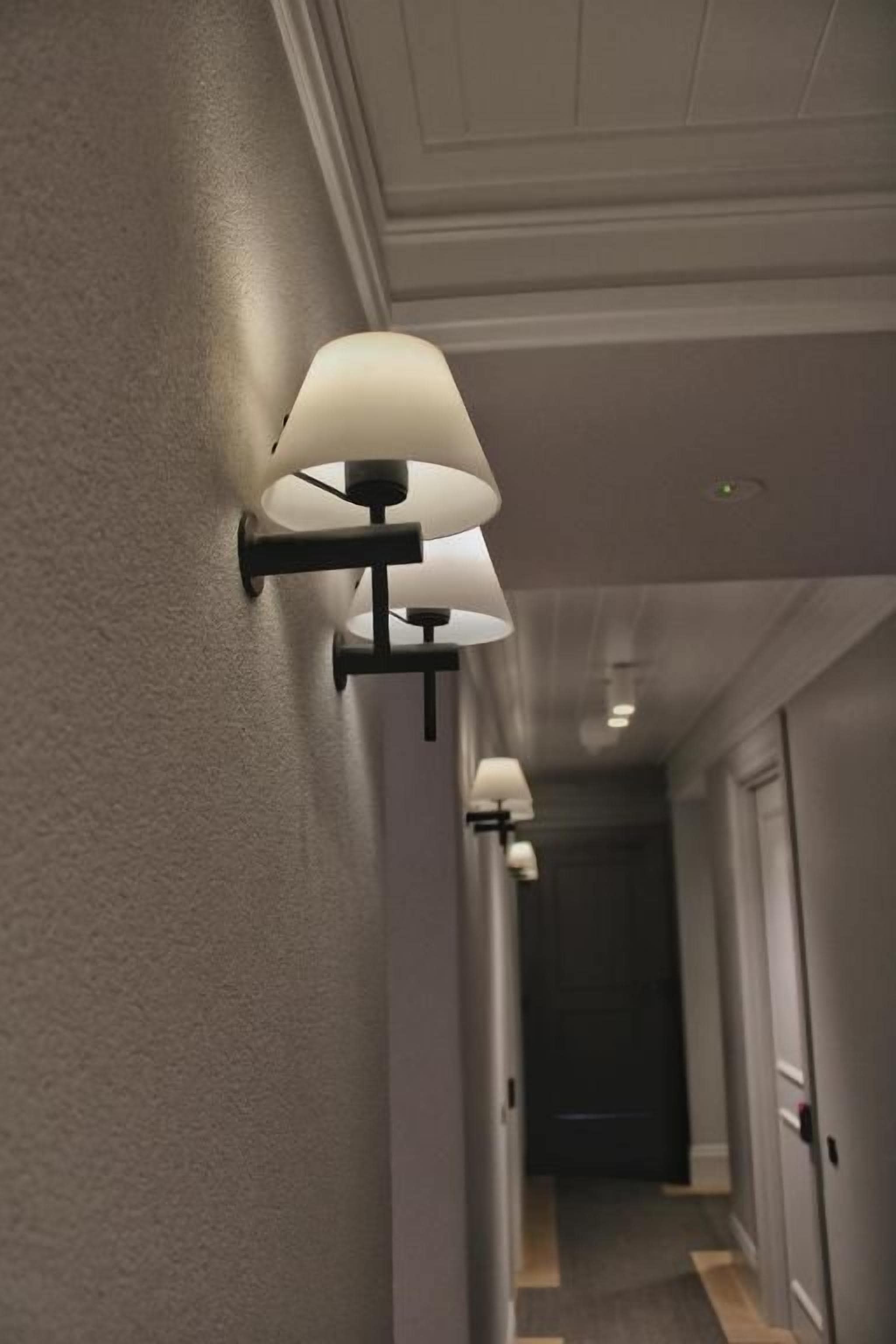 Un couloir avec des luminaires fixés au mur et une porte au fond.