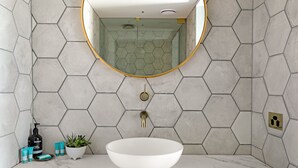A bathroom with a hexagonal tile wall, a white sink, a mirror with a gold frame, and toiletries on the counter. - The Bowral Hotel (Bowral)