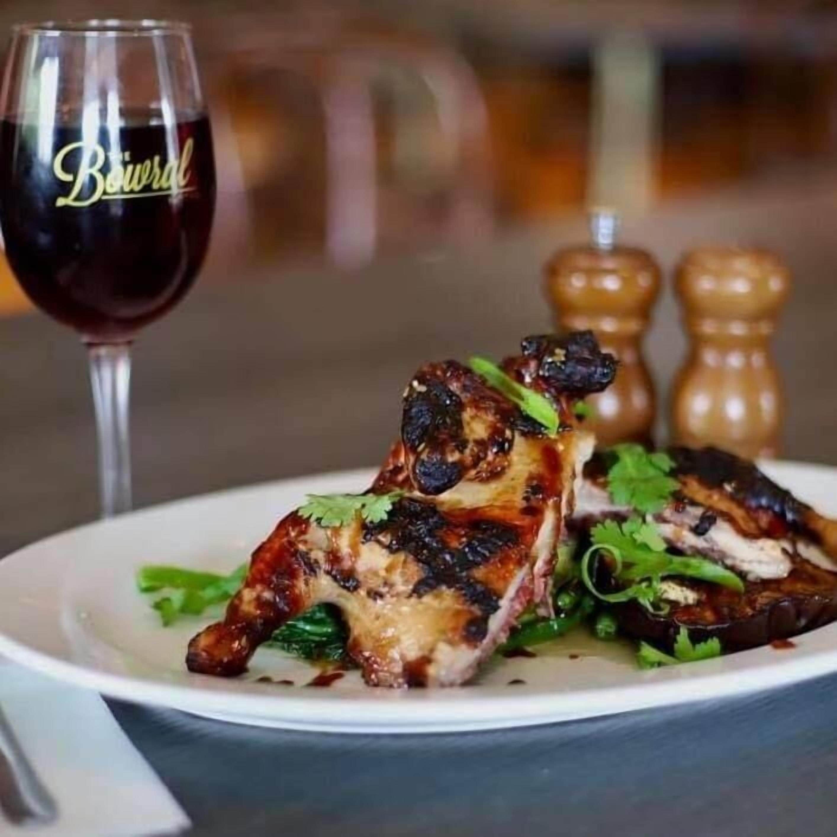 A plate of grilled chicken with herbs, a glass of red wine, and two salt and pepper shakers.