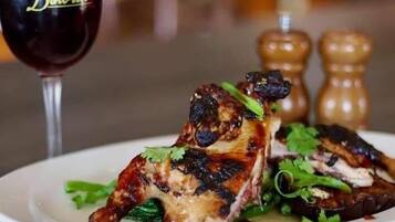A plate of grilled chicken with herbs, a glass of red wine, and two salt and pepper shakers.
