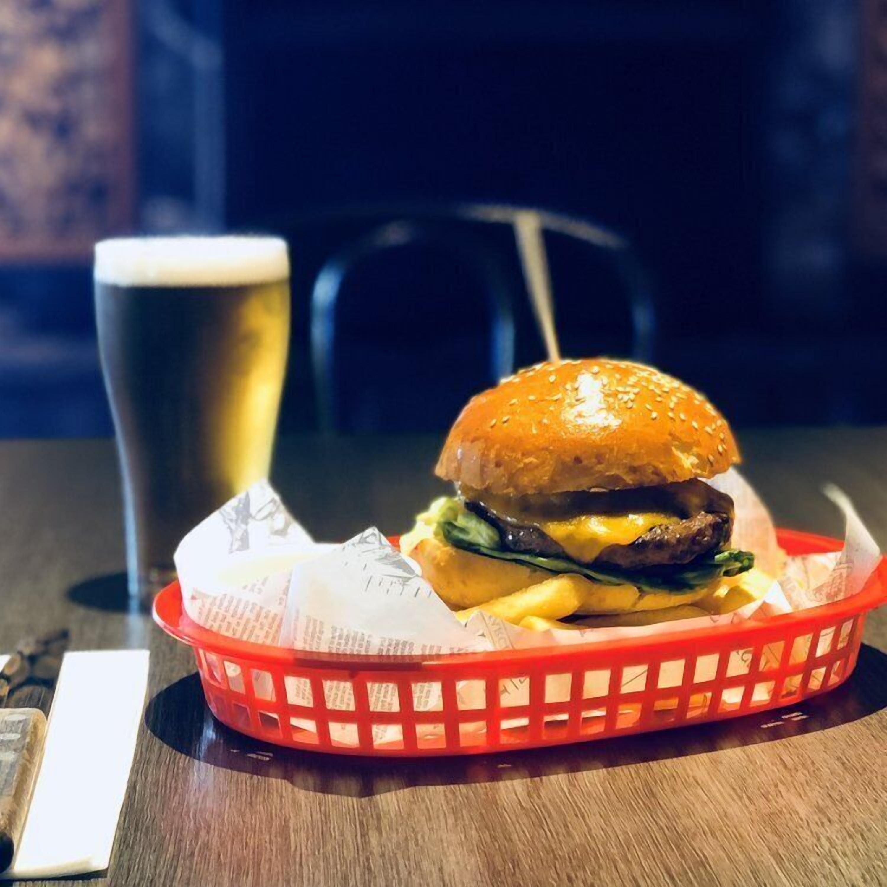 Una hamburguesa, patates fregides i un got de cervesa sobre una taula.