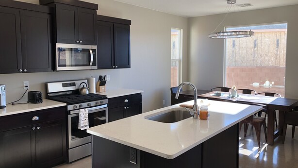 A modern kitchen with dark cabinetry, a stainless steel stove, and a large island with a sink. - MONTHLY RENTAL ONLY  (Hurricane)