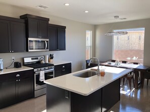 A modern kitchen with dark cabinetry, a stainless steel stove, and a large island with a sink. - MONTHLY RENTAL ONLY  (Hurricane)
