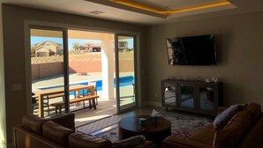 A living room with a sofa, a coffee table, a TV, and a sliding glass door leading to a patio with a pool. - MONTHLY RENTAL ONLY  (Hurricane)