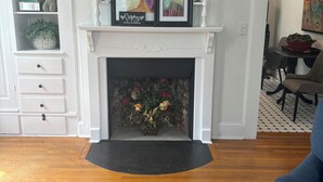 A living room with a white fireplace, a bookshelf, and a dining area with a patterned rug. - Charming Condo in Downtown Wilmington’s Historic District (Wilmington)