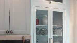 A kitchen with white cabinets, a microwave, a stove, and a glass-fronted cabinet with decorative items. - Charming Condo in Downtown Wilmington’s Historic District (Wilmington)