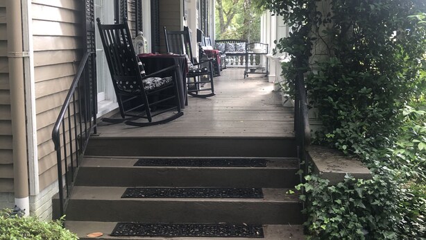 A porch with steps leading to a seating area, surrounded by greenery and a building with shutters. - Charming Condo in Downtown Wilmington’s Historic District (Wilmington)