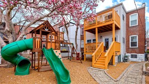 A playground with a slide and climbing structures, surrounded by a brick building and a tree with pink blossoms. - Family Friendly , Fully Renovated 3BR Luxury Home. Centrally located in St.Louis (St. Louis)