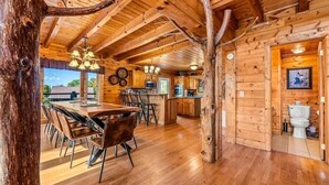 A rustic cabin interior with a wooden dining area, kitchen, and bathroom.
