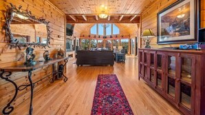 A cozy log cabin interior with a dark sofa, wooden walls, a large mirror, and a framed picture on the wall.