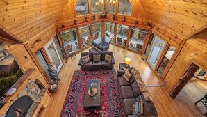 A spacious loft-style room with a large wooden ceiling, a piano, a fireplace, and multiple windows offering views of the outdoors.