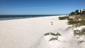 Una playa con cielo despejado, orilla arenosa y edificios al fondo.